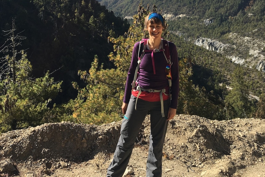 A woman wearing hiking clothes and smiling and standing in front of mountains.