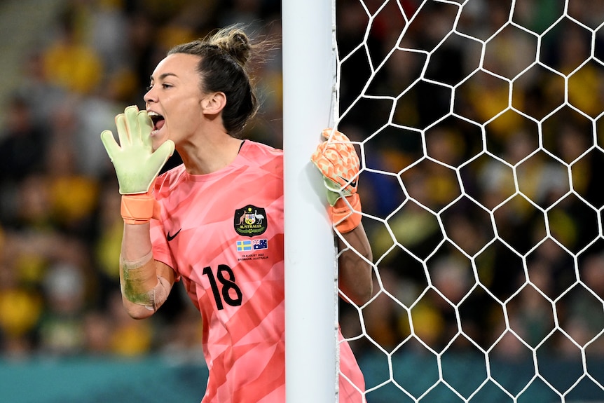 An Australian women's soccer goalkeeper calls out to her defence as she holds on to the goal post during a game.