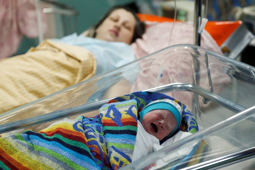 A newborn baby cries next to his mother while taking shelter in a basement