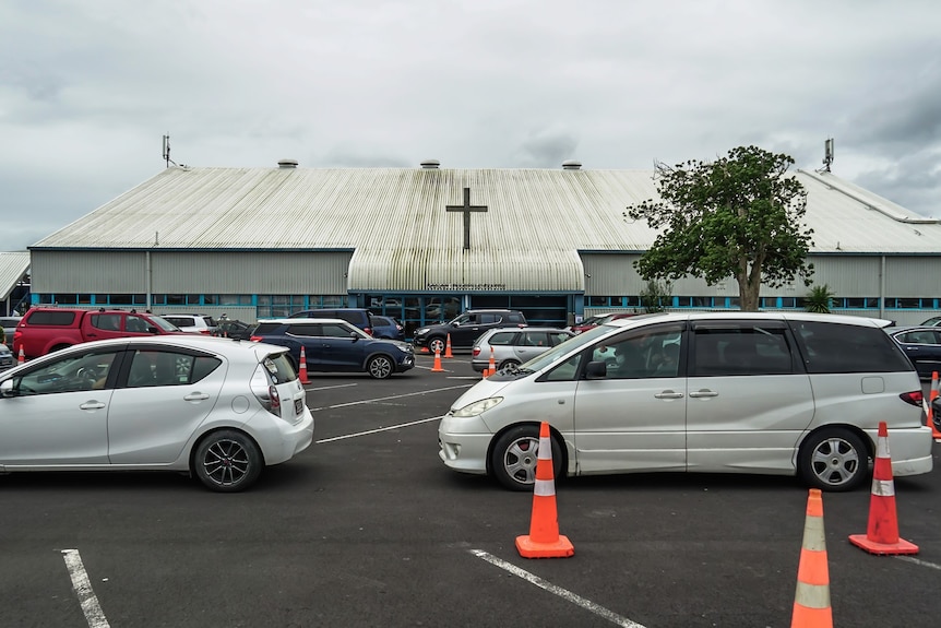 Cars line up in front of a large church building with a cross on the front. 