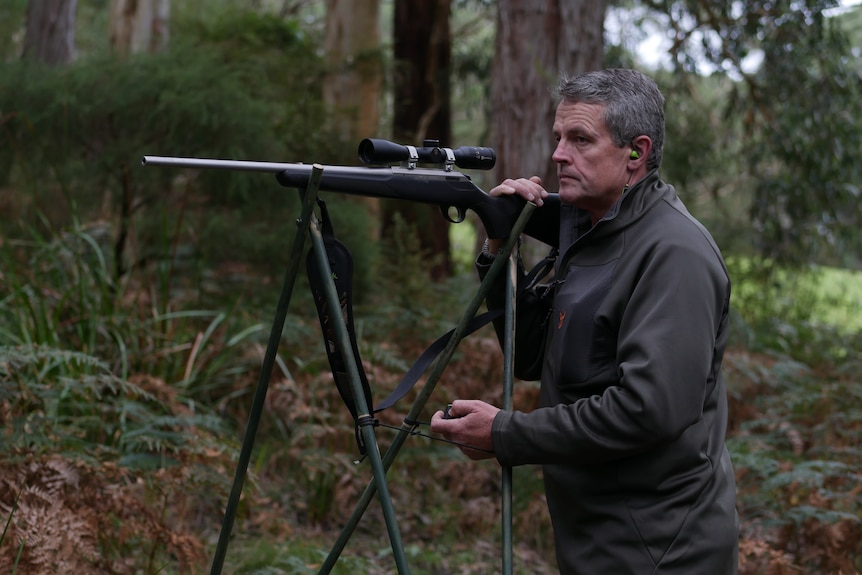 a gray haired man positions a rifle on a makeshift stand
