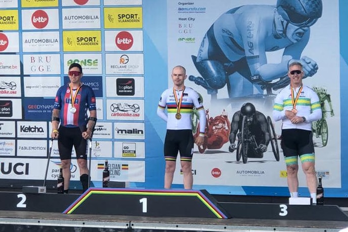 Three male cyclists stand on a podium with medals around their necks.