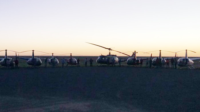 A dozen helicopters are parked on the tarmac at Richmond aerodrome, with the sun setting in the background