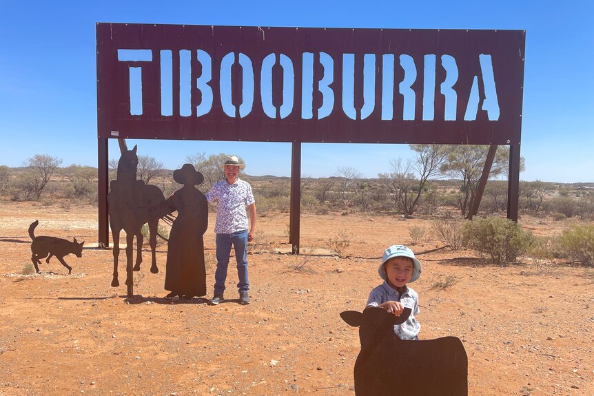 A man and child stand in front of a sign reading Tibooburra.