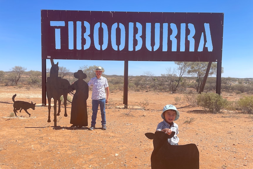 A man and child stand in front of a sign reading Tibooburra.