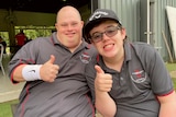two young men give a thumbs up to the camera