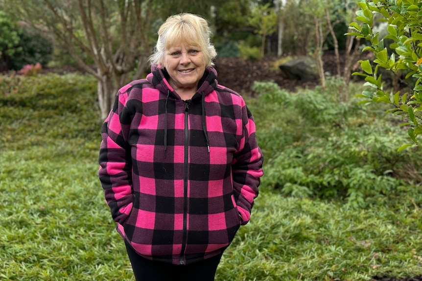 Yvonne is standing in her garden wearing a black and pick checked jacket