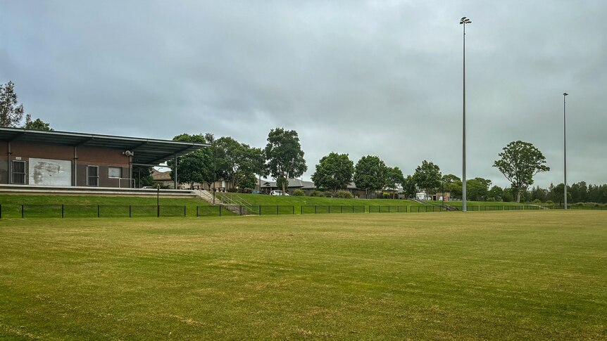 A rugby field with clubrooms and lights in the background