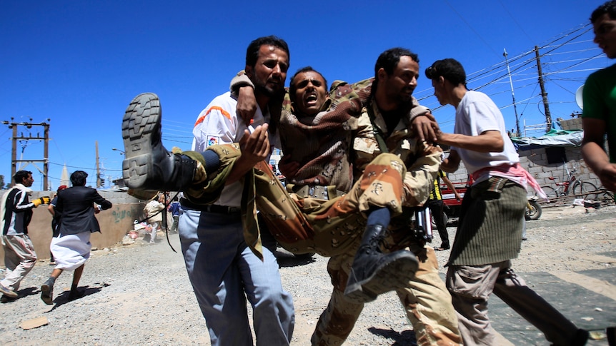 Medics carry a wounded defected soldier after clashes with police in Sanaa