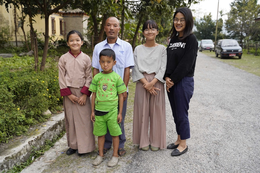A family of one man, three daughters and a son stand outside a brick home in Bhutan