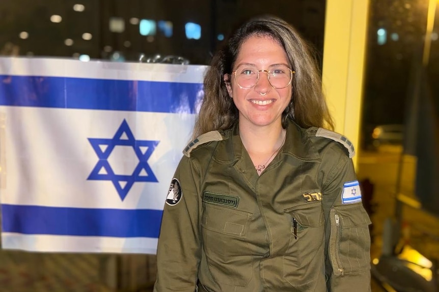 Israeli woman in military uniform with the flag behind her.