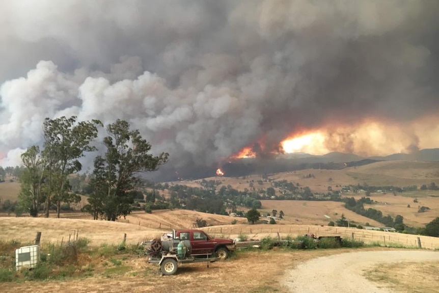 A bushfire produces huge orange flames and thick smoke over hills near Buchan.