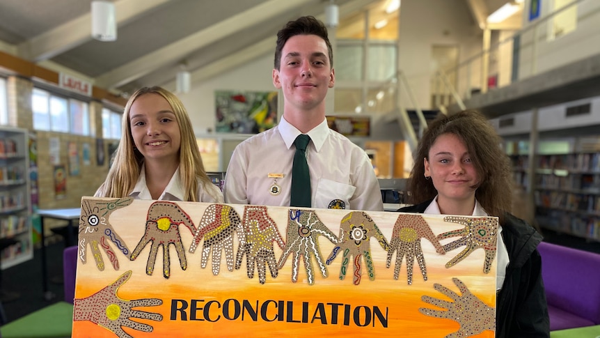 Two young women and a young man hold a painting which says reconciliation