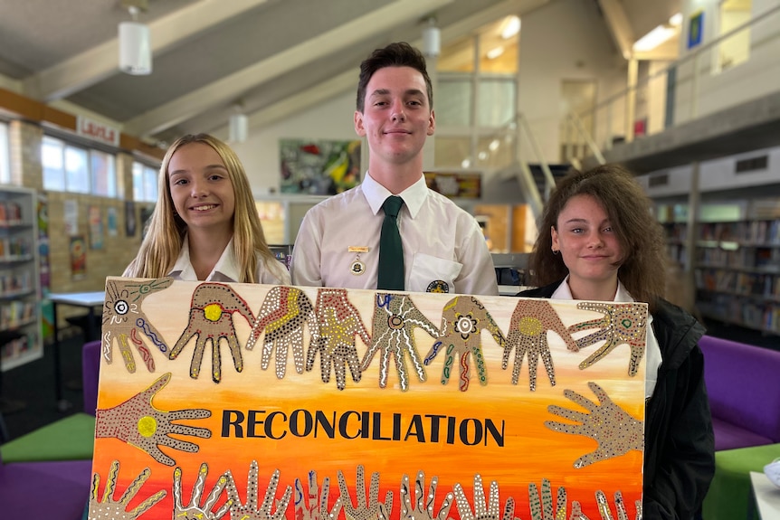 Two young women and a young man hold a painting which says reconciliation