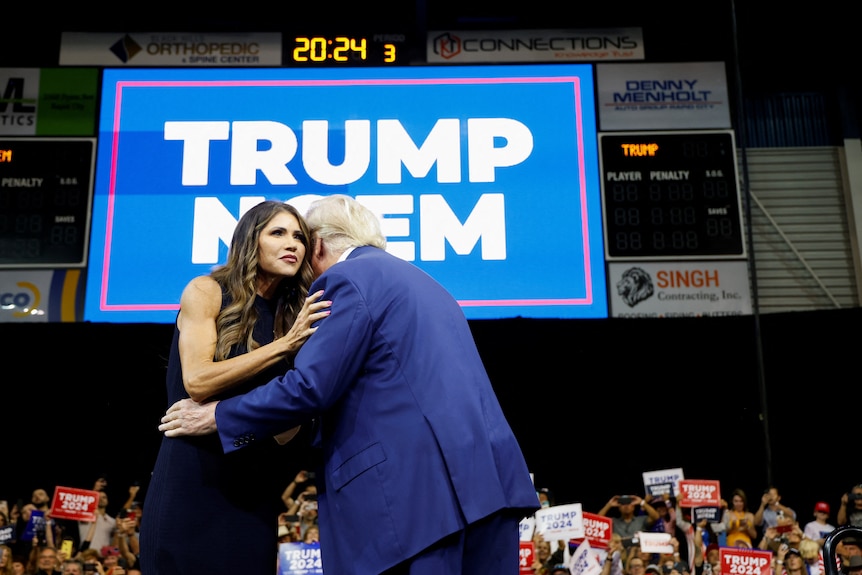 Donald Trump hugs South Dakota Governor Kristi Noem on a podium at a rally