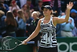 Ash Barty smiling and holding her tennis racquet in her right hand and waving with her left.