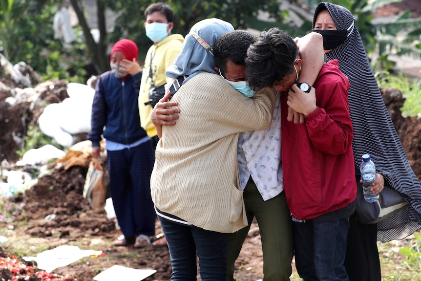 A man and woman embrace a sobbing man at a graveyard 