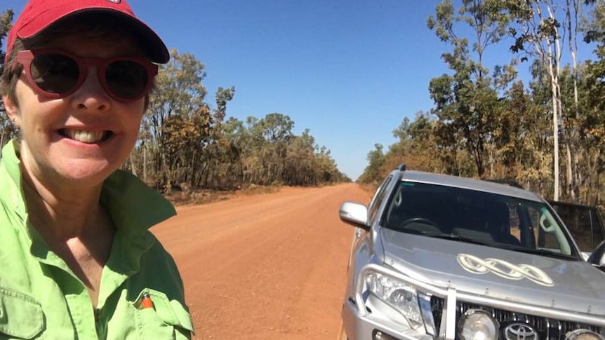 Woman in red cap stands on dirt road with silver car