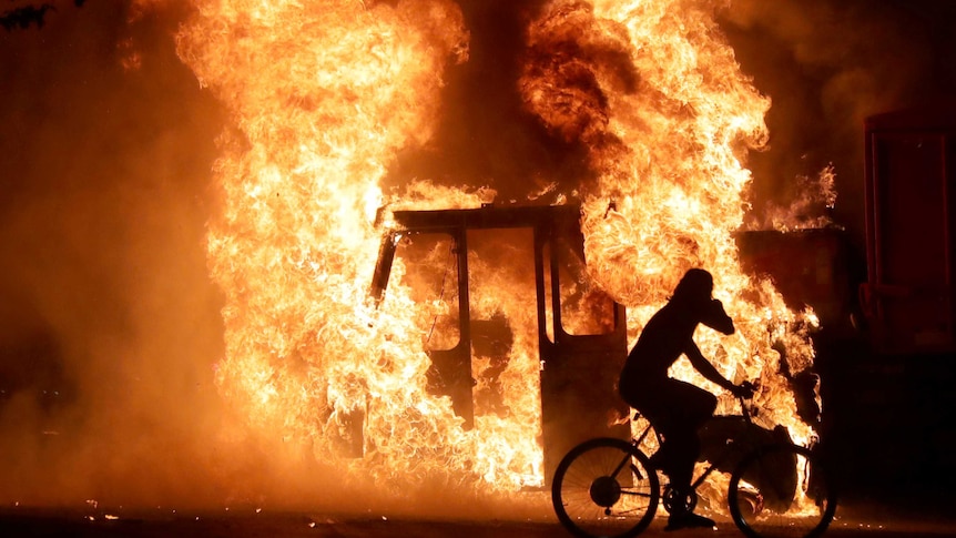 A man on a bike rides past a city truck on fire outside the Kenosha County Courthouse in Kenosha, Wisconsin.