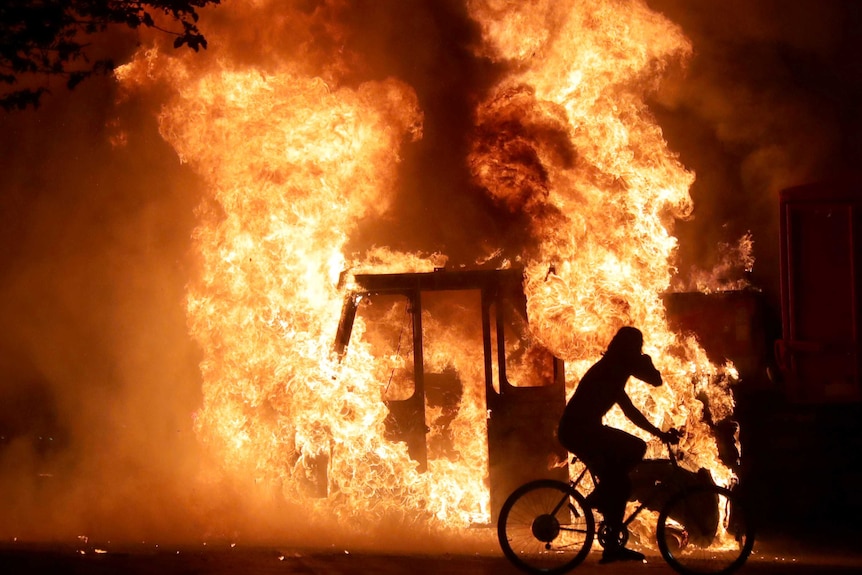 A man on a bike rides past a city truck on fire outside the Kenosha County Courthouse in Kenosha, Wisconsin.