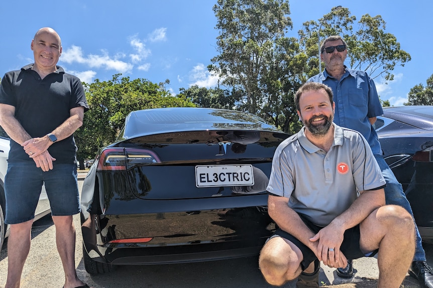Three men stand or sit near a Tesla with the numberplate EL3CTRIC.
