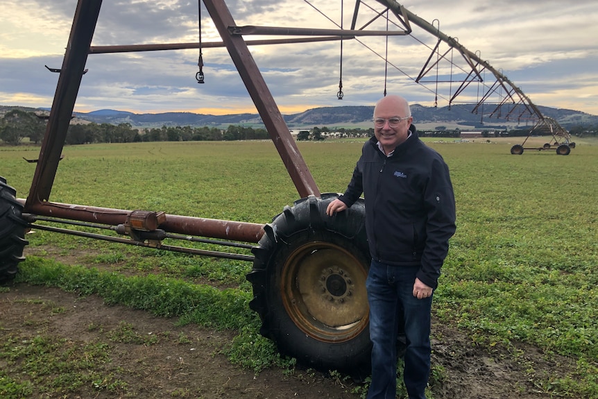 An older man stands in front of an irrigation machine in a lush field.