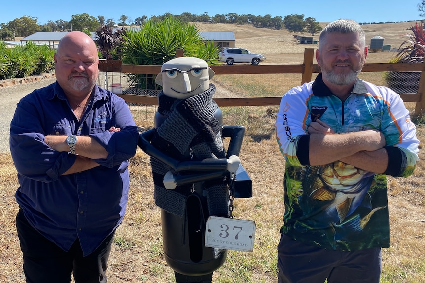 Two men stand with folded arms either side of a mailbox, which also has folded arms