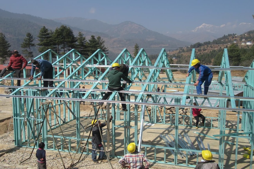The steel frame of a partly constructed earthquake-proof classroom with six people working on it.
