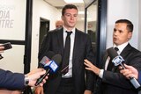 Essendon player Conor McKenna, wearing a suit, walks towards a group of media members with microphones at the AFL tribunal.