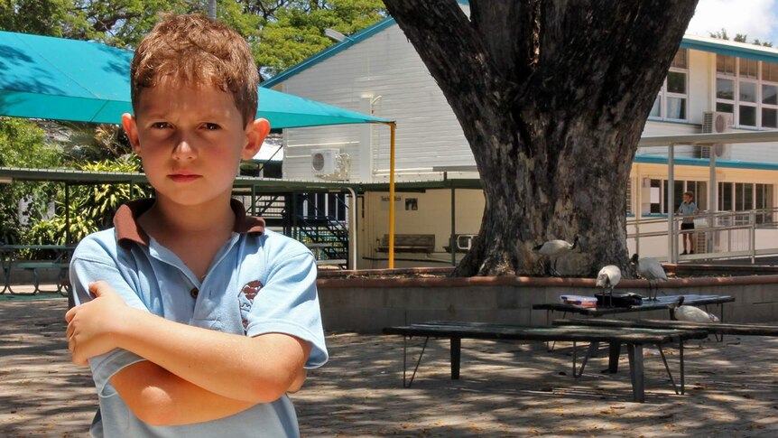 A child stands with arms crossed in front of the school quadrangle with ibis in the background
