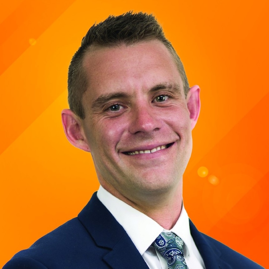 Headshot of man with spikey hair in front of a bright orange background. 