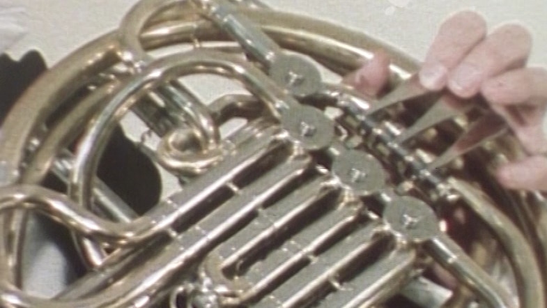 A close-up of a French horn with fingers pressing the keys.