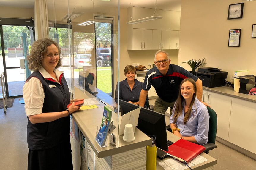 Four people standing around a reception desk, smiling at camera 