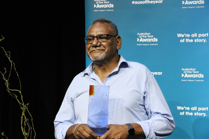 a middle-aged aboriginal man wearing glasses and a collared shirt accepts an award