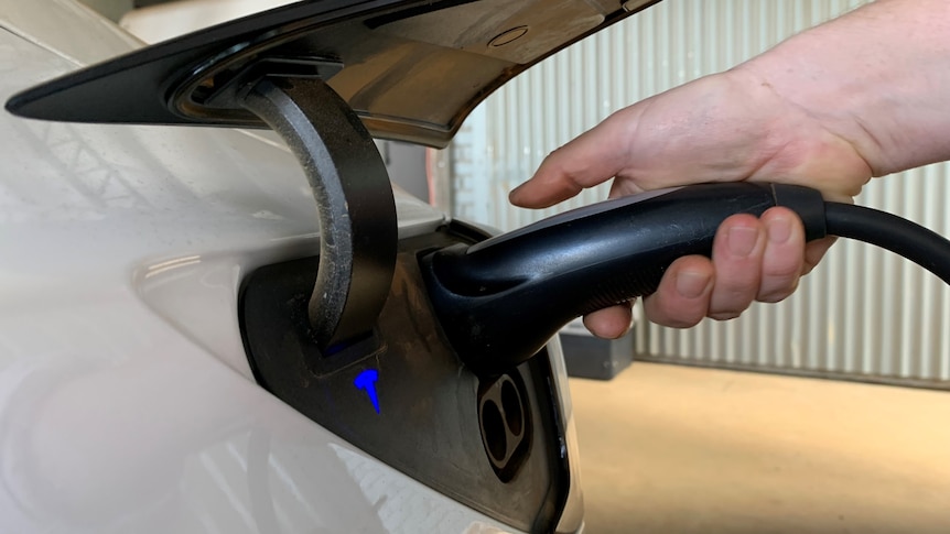 A hand holding an electric vehicle charger and plugging it into the car
