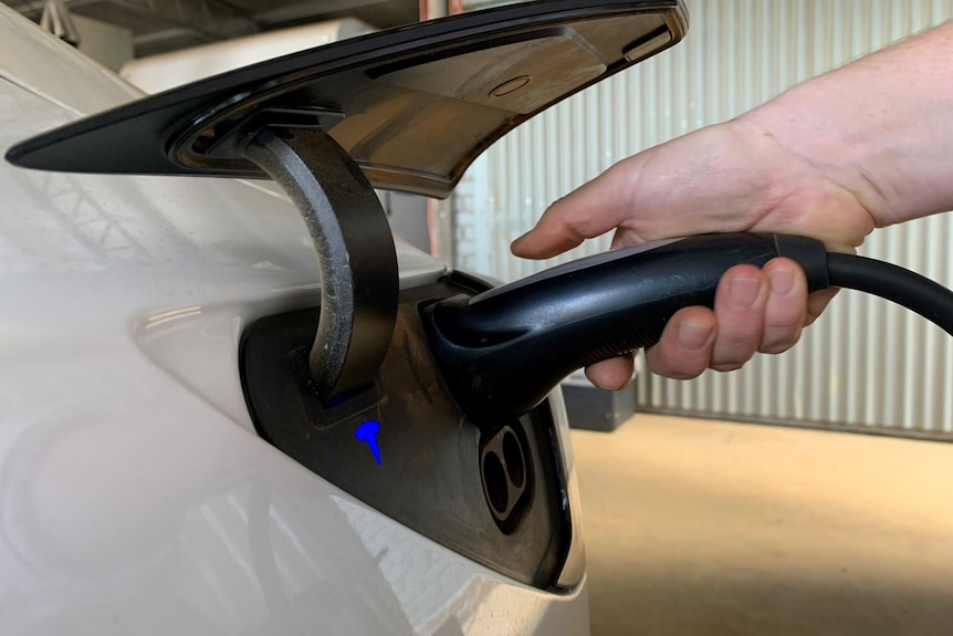 A hand holding an electric vehicle charger and plugging it into the car