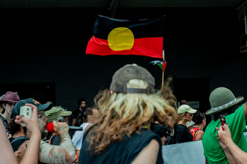 An Aboriginal flag waving in the wind above a crowd of people. 
