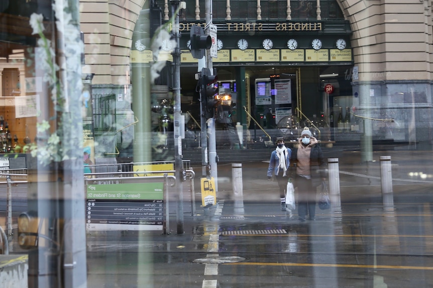 People are seen in the reflection of a window walking outside Flinders Street Station on a rainy day.