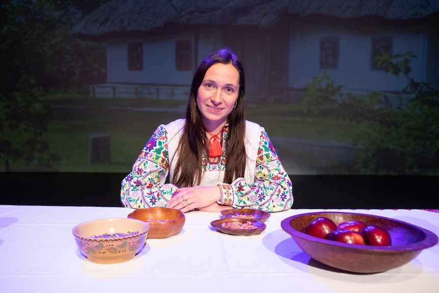 A woman with long brown hair sits at a table with props
