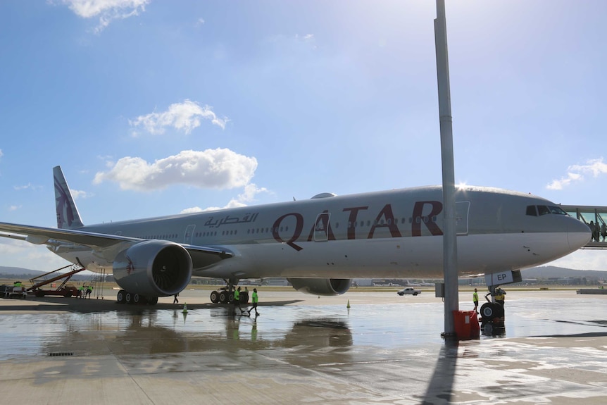 A Qatar Airways at the gate at Canberra Airport on a clear, sunny day.