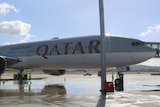A Qatar Airways at the gate at Canberra Airport on a clear, sunny day.