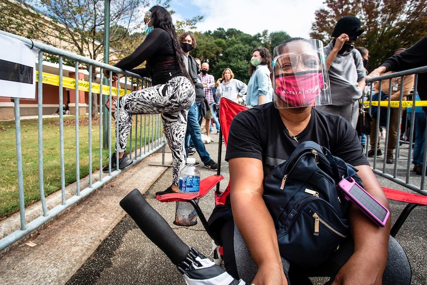 An unidentified woman wearing a face mask and shield sits as she waits in line for early voting