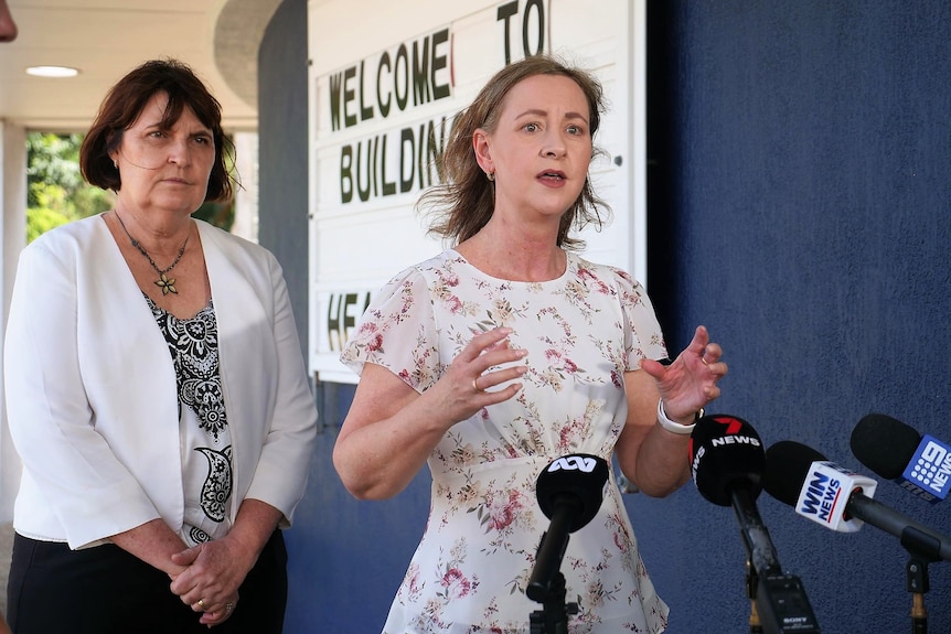 A woman in a while floral dress standing next to a woman wearing a white jacket and black pants.