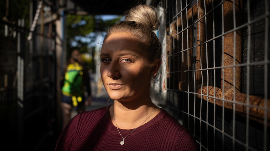 Woman standing next to a fence with shadows across her face. 