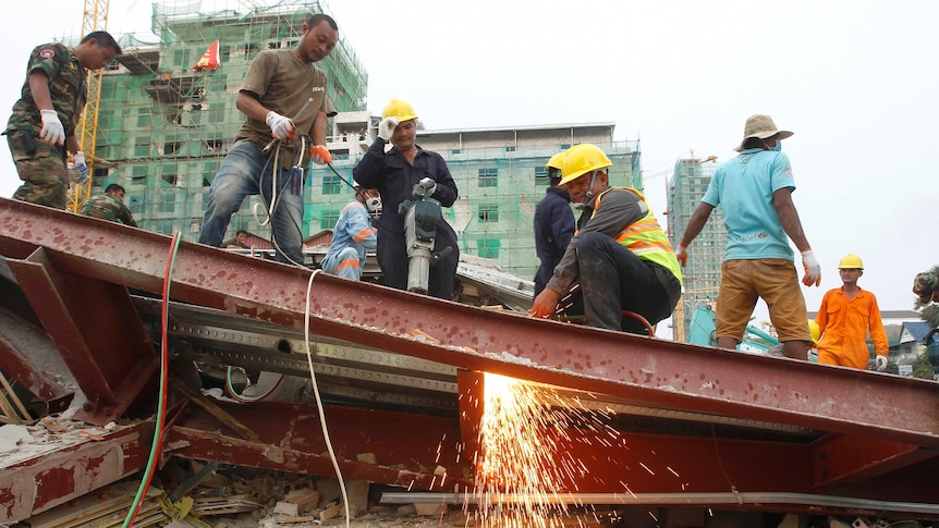 Rescue workers use an angle grinder to cut into the collapsed steel shell of a multi-storey building.