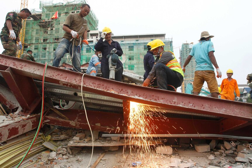 Rescue workers use an angle grinder to cut into the collapsed steel shell of a multi-storey building.