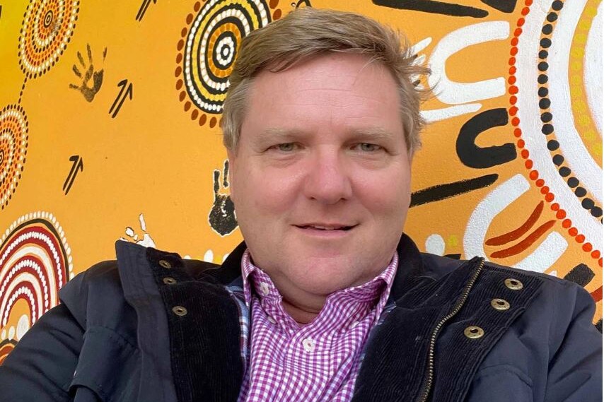 a man sitting in front of an indigenous dot artwork