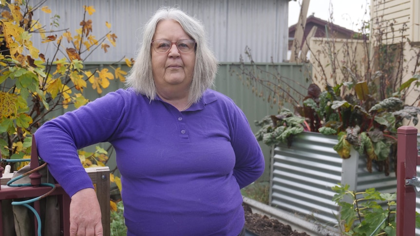 woman with glasses and purple shirt stands in front of vegetable garden