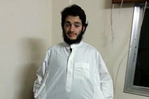 Man with black hair and beard wears white gown stands in carpeted room