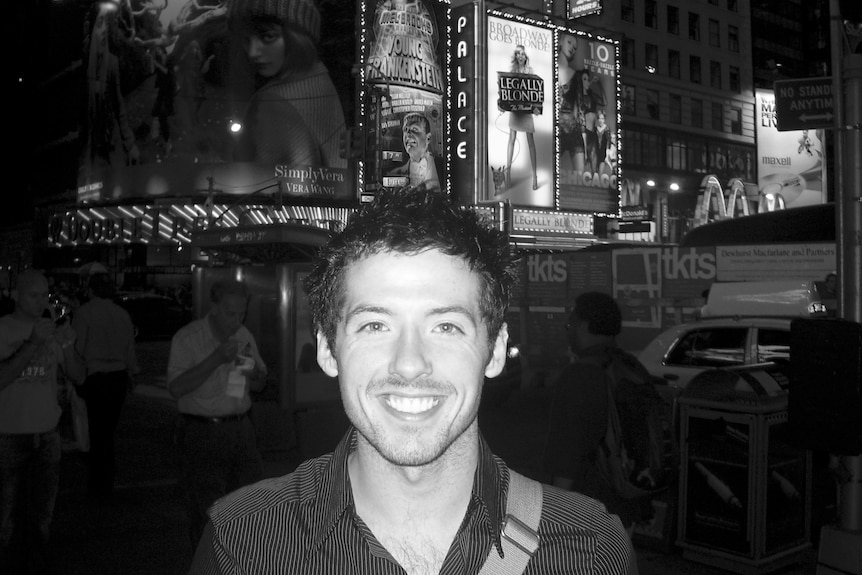 Caleb smiles as he stands in front of billboards promoting upcoming musicals in an entertainment precinct.